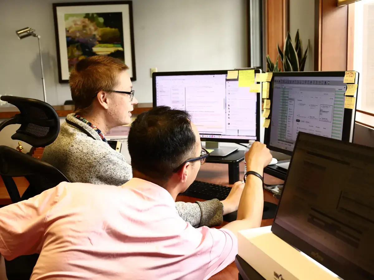 Two members of the B&A team working together at their computer monitors