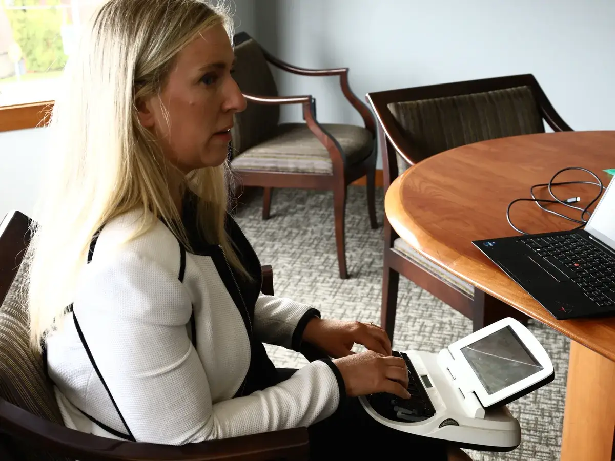 Co-owner Sarah Fitzgibbon writing on her stenotype machine in a B&A Tacoma conference room, with a laptop open on the table
